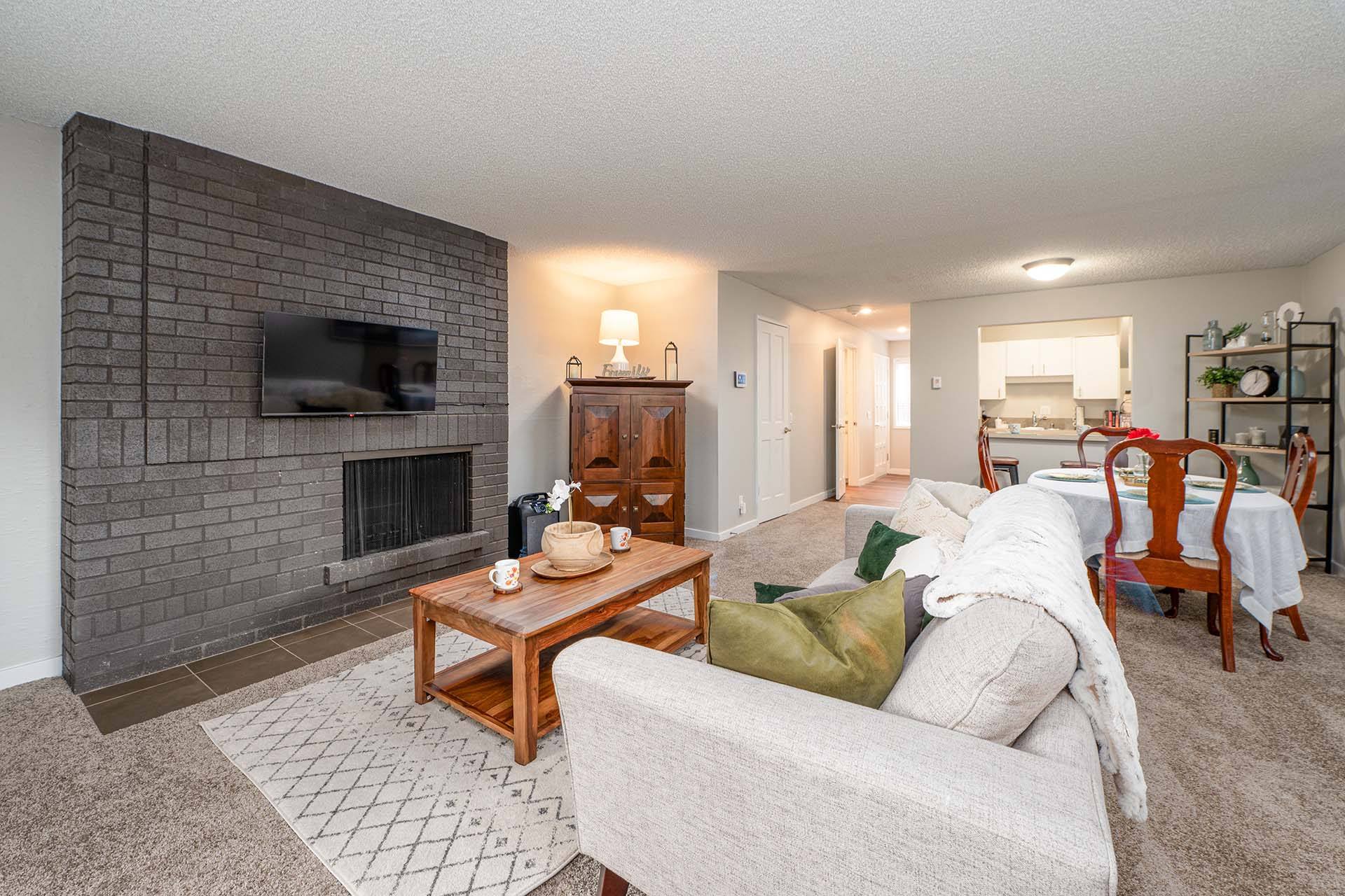 A living room with a grey couch, a wooden coffee table, a fireplace, and a television mounted on a brick wall.