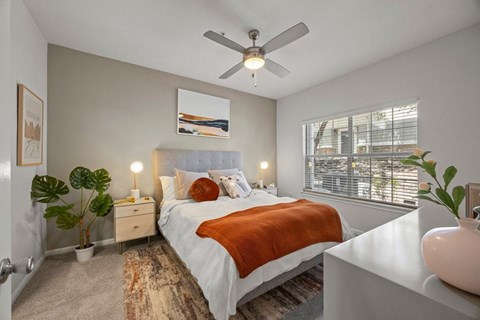 A bedroom with a bed, a ceiling fan, and a window with blinds.