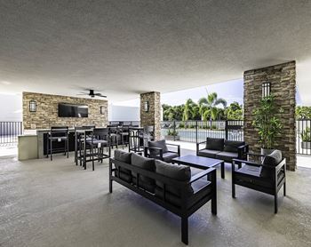 A modern outdoor patio with black furniture and a stone wall.