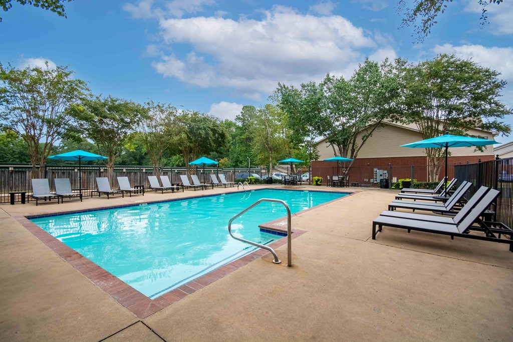 our resort style swimming pool is surrounded by lounge chairs and umbrellas