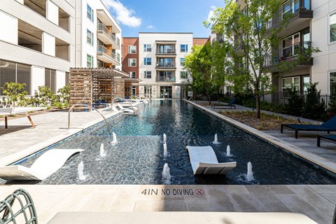 Two-Bedroom Luxury Apartments in Fort Worth, TX - The Union at River East - Swimming Pool with Small Fountains, In-Pool Loungers, Sun Loungers, Pergolas, Trees, and Metal Fence.