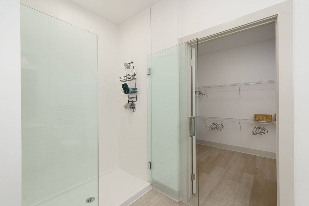 A white bathroom with a glass shower door and a white closet.