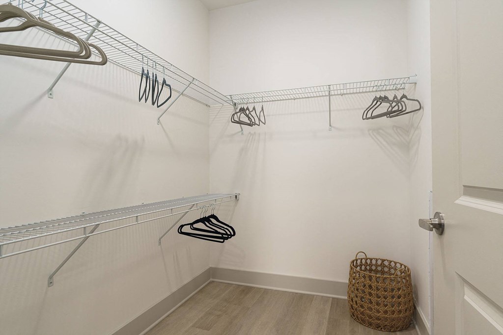 A white closet with clothes hanging on a rack and a basket on the floor.