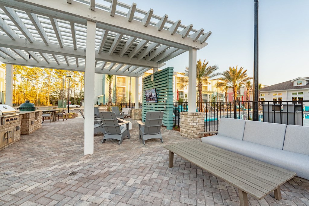 A patio with a white pergola and grey chairs.