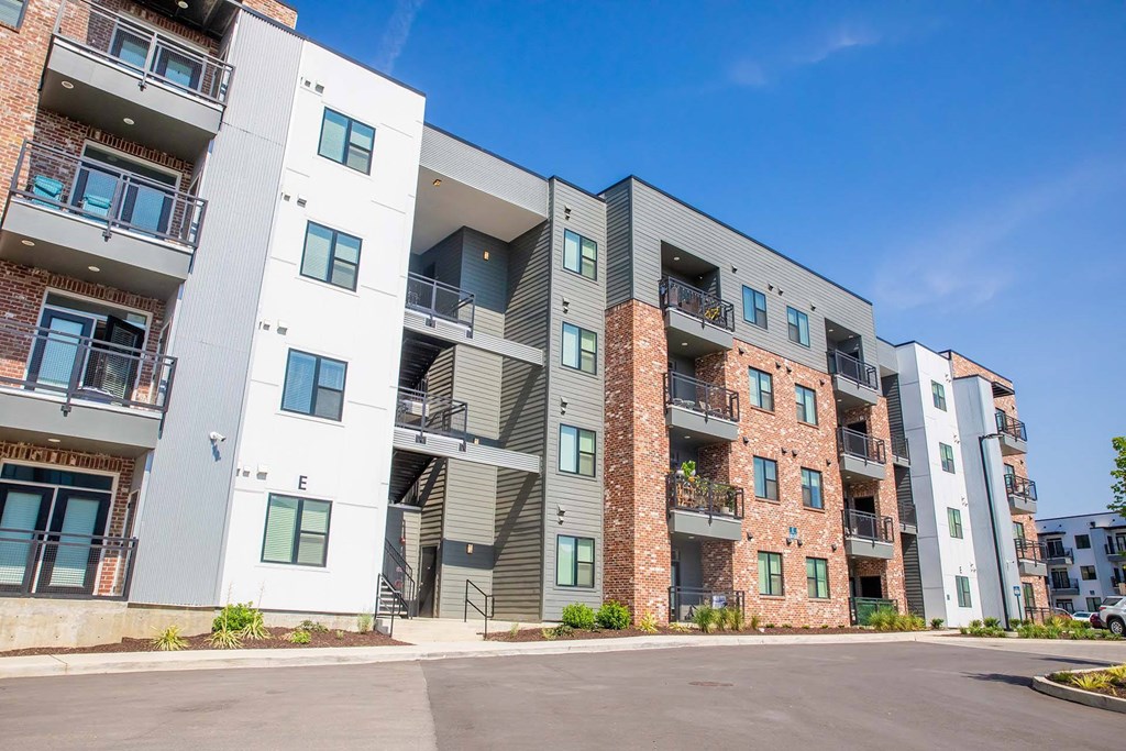 Luxury Apartments for Rent in Nashville TN - Sterling Nashville West - Property Exterior with Brick, White, and Grey Walls, Showcasing Balconies, Stairwells, and Street, with Landscaped Plants at Base Level