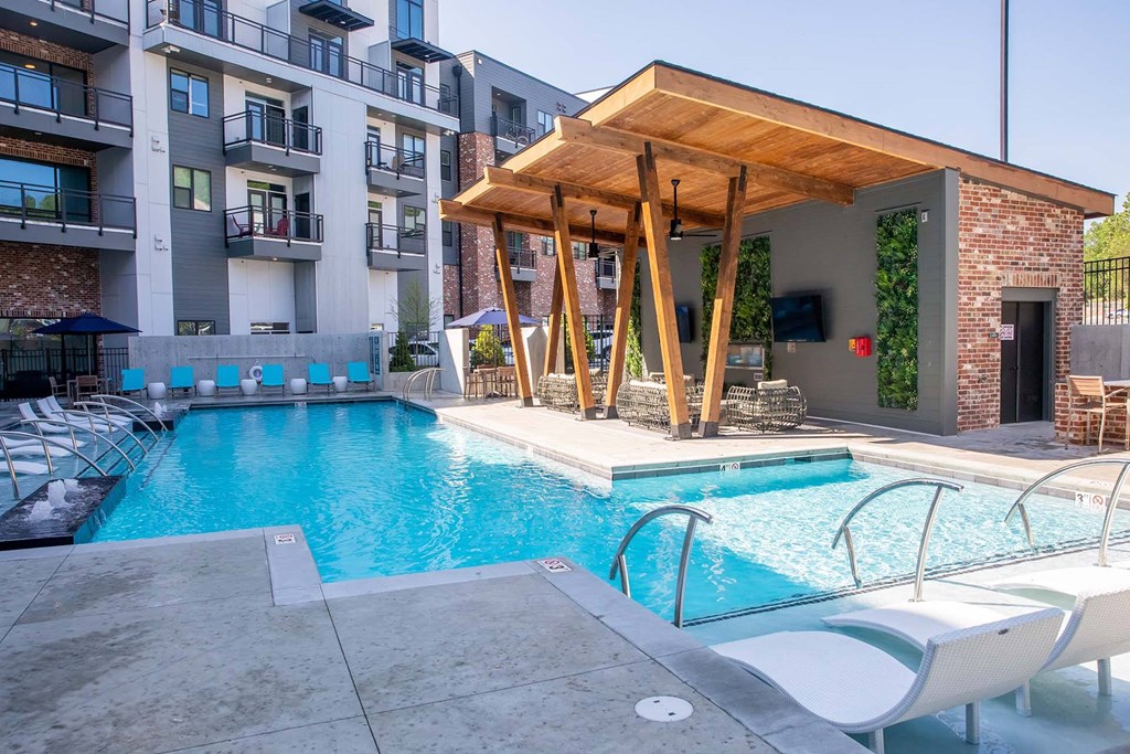 Pet-Friendly Apartments in Nashville TN - Sterling Nashville West - Gated Pool Area with Submerged and Poolside Lounge Seating, Covered Seating Area with Plant Wall and TVs, and View of Building Exterior in Background
