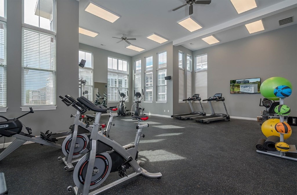 A gym with a row of stationary bikes and a fan.