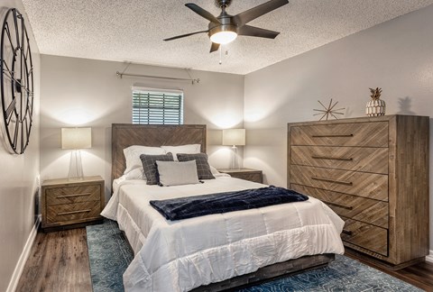 2-Bedroom Apartments in Riverview, FL - Sherwood Oaks Apartments - Cozy Bedroom With Wood Bed Frame, Ceiling Fan Light, Matching Nightstands, Textured Rug, and Chevron Front Dresser.