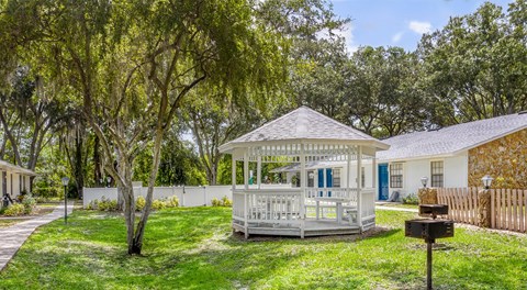 A gazebo is surrounded by a white picket fence and trees.