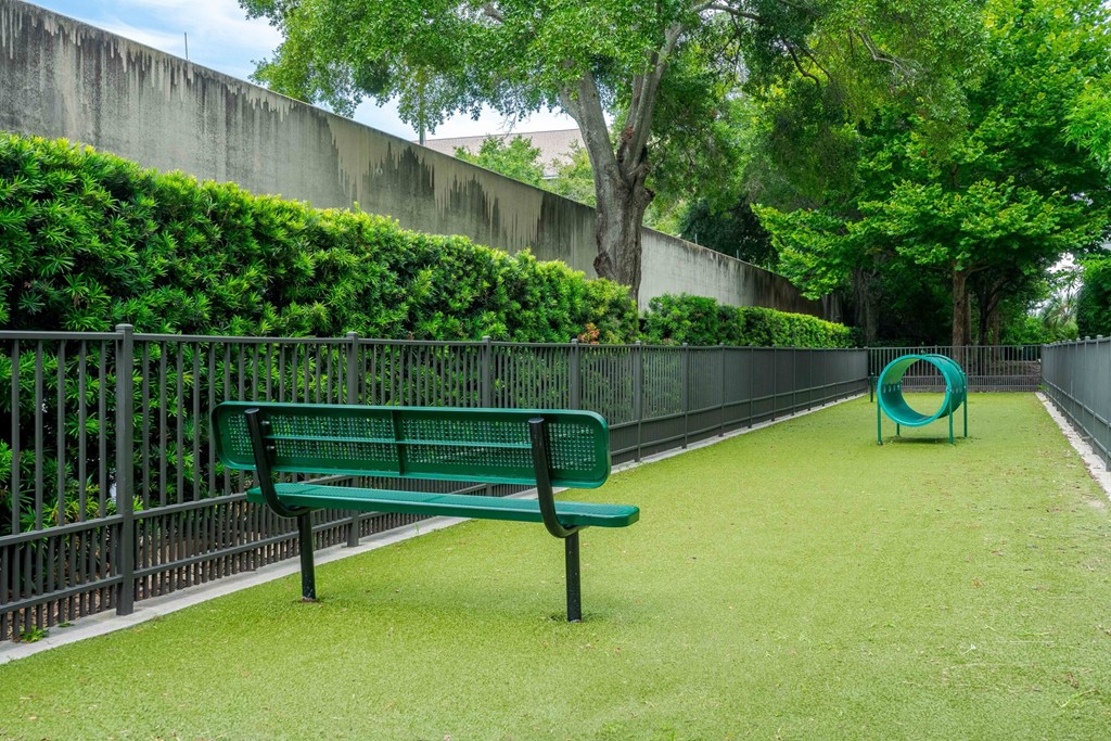 A green bench sits on a green lawn next to a green playground equipment.