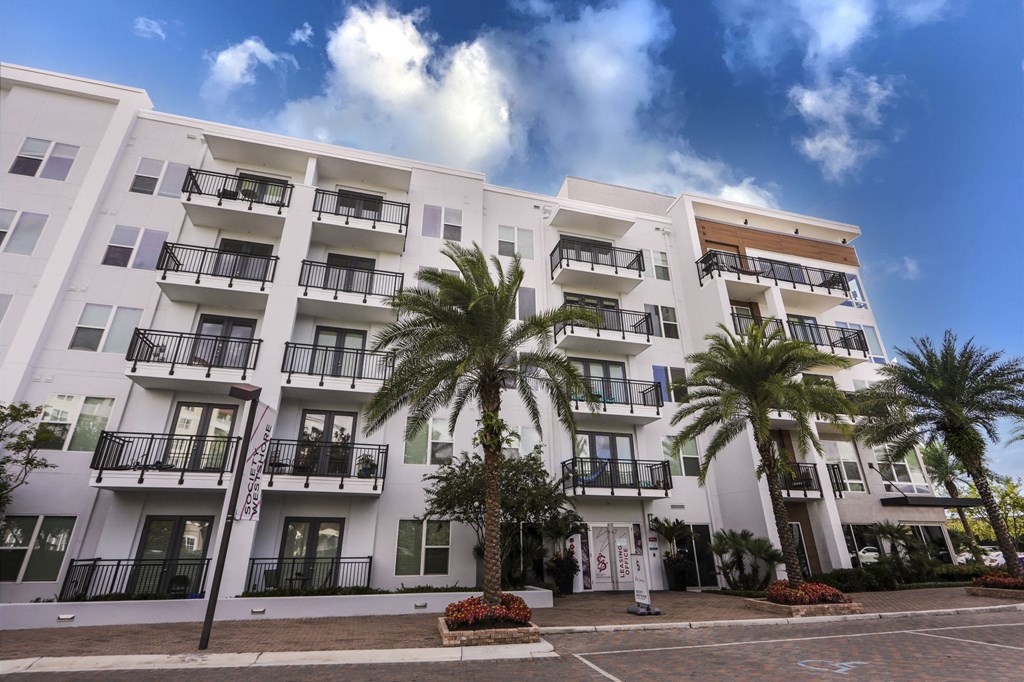 Luxury Apartments in Tampa FL - Society Westshore - Property Exterior Showcasing Balconies, with Bright White Walls, Palm Trees, Landscaping, and Street View