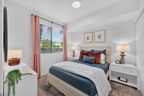 A bedroom with a bed, nightstand, and window with curtains.