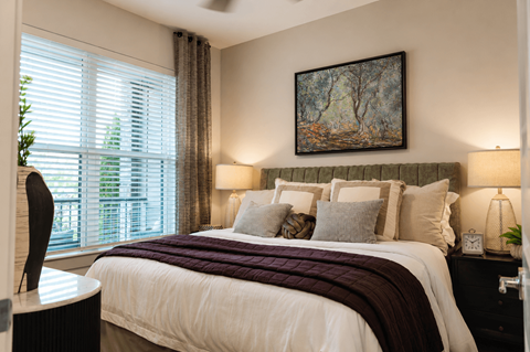 Dog-Friendly Luxury Apartments in Kennesaw, GA - Rue 108 Apartments - Bedroom With Upholstered Bed, Nightstands, Lamps, Wall Art, and Large Window with Coverings.