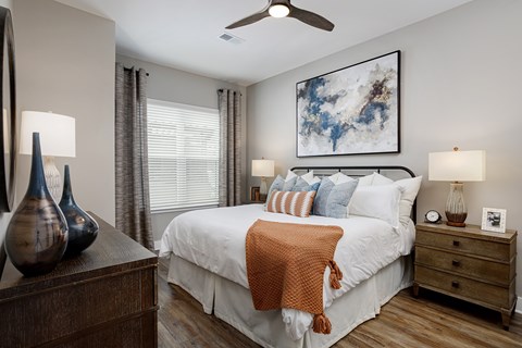 A bedroom with a large bed, a ceiling fan, and a painting on the wall.