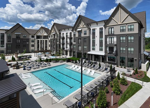 A large swimming pool is surrounded by lounge chairs in front of a large building.