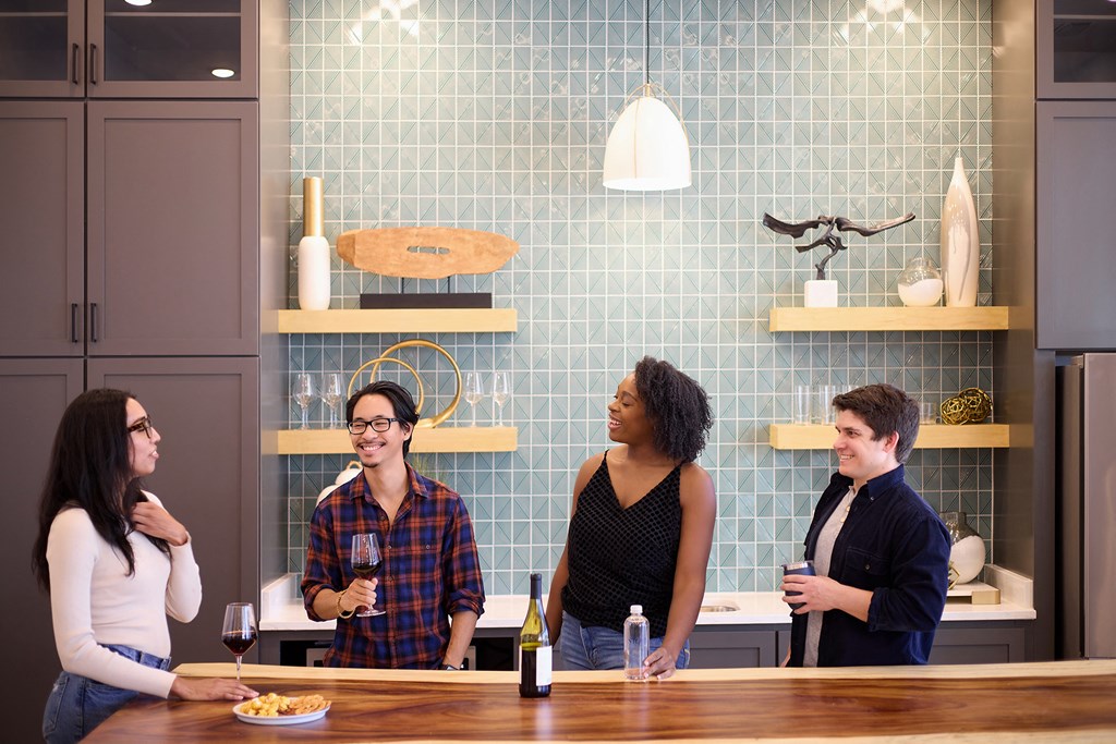 a group of people standing in a kitchen talking and drinking wine