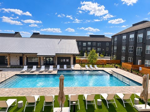 A pool surrounded by chairs and umbrellas with a building in the background.