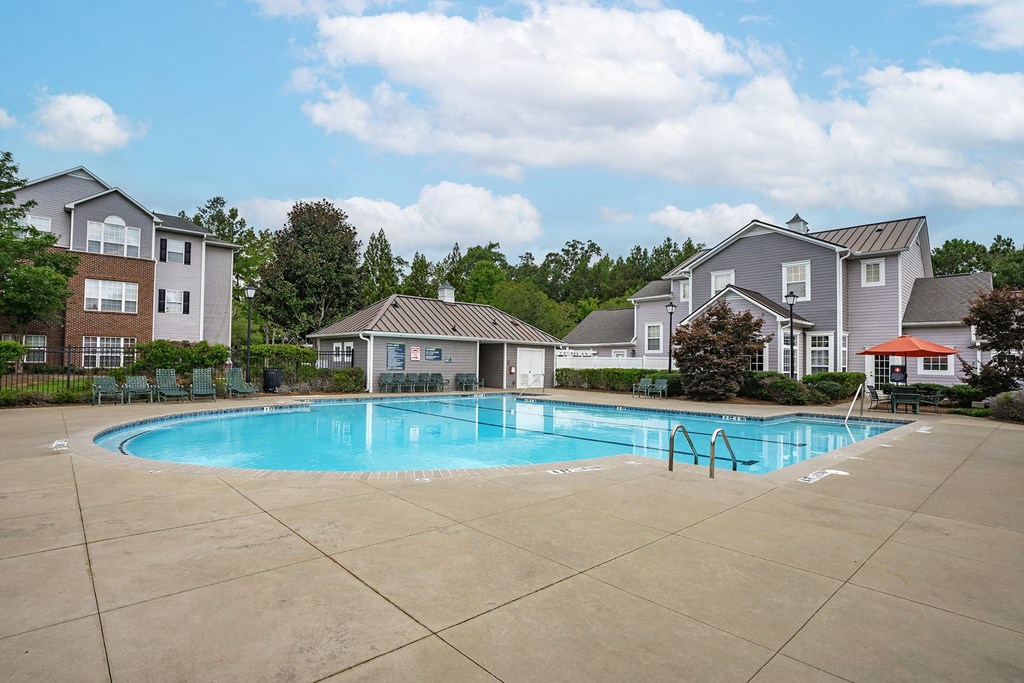 A swimming pool surrounded by a concrete patio and residential buildings.