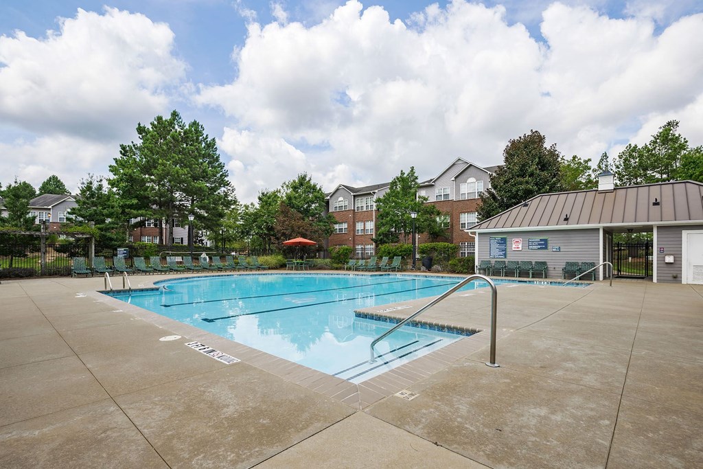 A large outdoor swimming pool surrounded by a concrete patio and a metal fence.