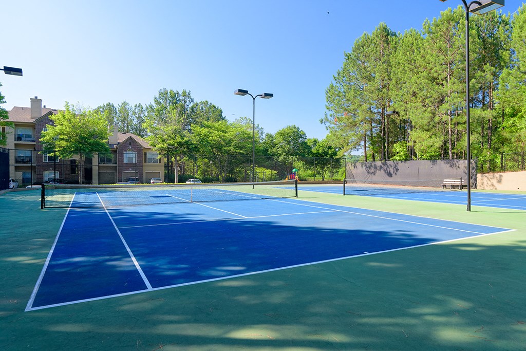 two tennis courts with trees and buildings in the background