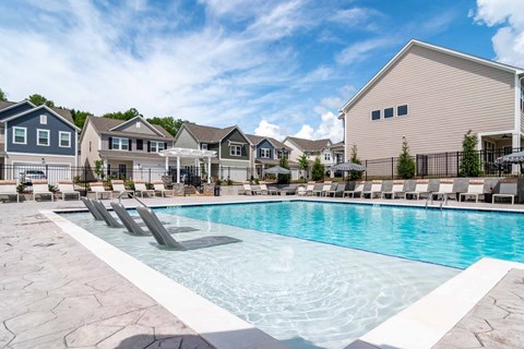 A swimming pool with lounge chairs in front of a row of houses.