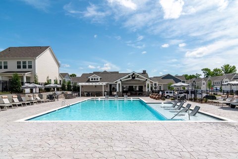 A swimming pool surrounded by a patio with chairs and a building in the background.