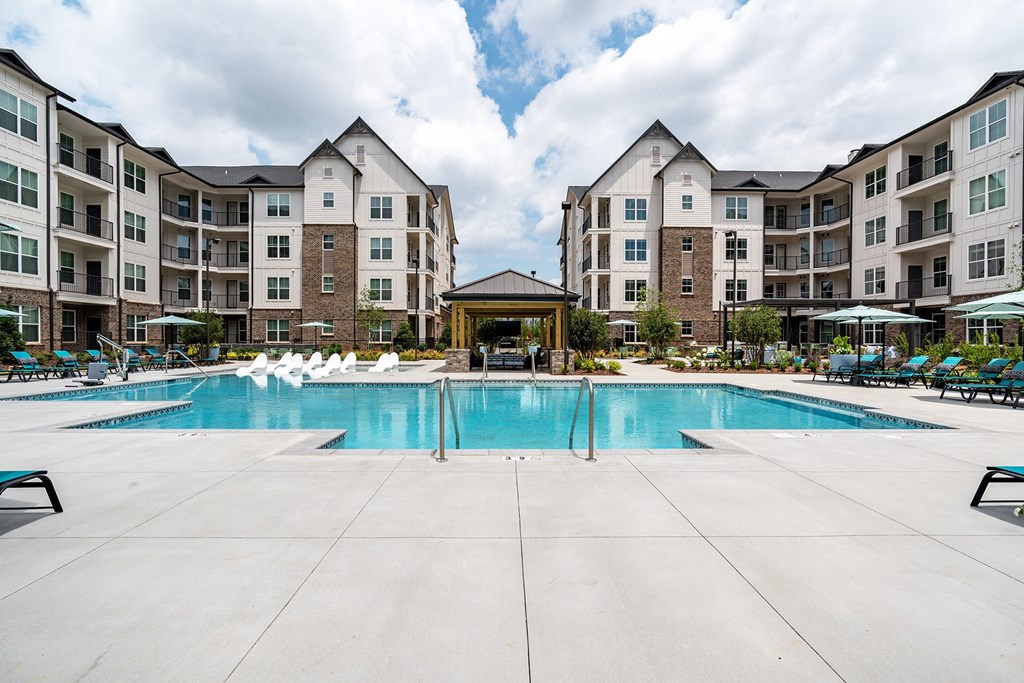 Apartments in Madison, Alabama with In-Unit Washer and Dryer - The Dempsey - Resort-Style Pool with Sunshelf Surrounded by Lounge Seating and Apartment Buildings.