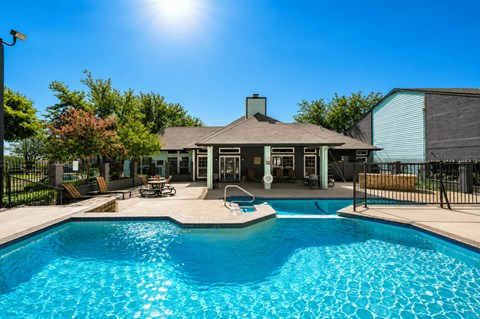 A pool in front of a house with a sunny sky.