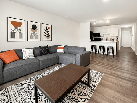 A living room with a grey couch, a coffee table, and a bar area in the background.