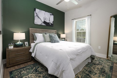 Apartments With Boat Parking in Panama City, FL - The Tyde Apartments - Bright Bedroom With Green Accent Wall, Plush Bed, Ceiling Fan, Nightstands, Lamps, and Large Window With Sheer Curtains.