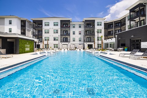 Apartments in Panama City Beach, FL, With In-Unit Washer and Dryer - The Tyde Apartments - Resort-Style Swimming Pool With Wide Sundeck, Lounge Chairs, and Modern Apartment Buildings Surrounding The Water.