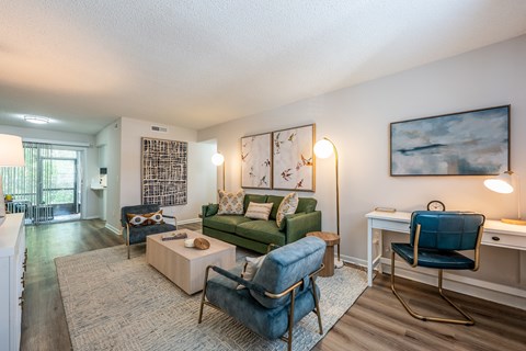 A living room with a green couch, a blue chair, and a painting on the wall.