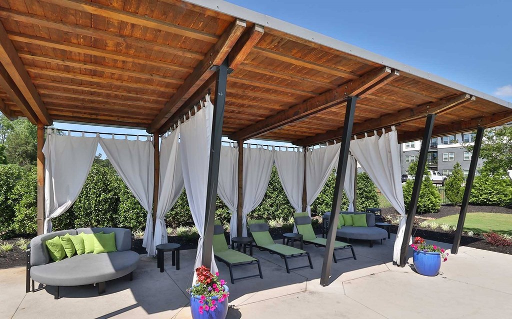 A wooden patio with white curtains and green cushions.