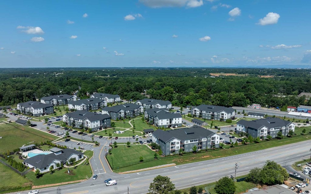 A large apartment complex is surrounded by trees and a road.