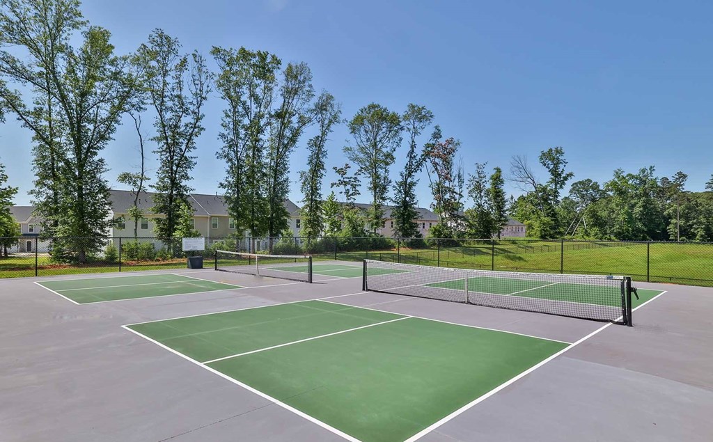 A tennis court surrounded by trees and a fence.