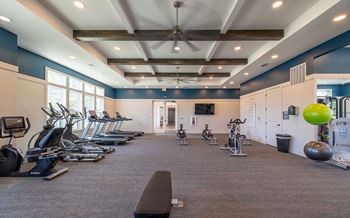 A gym with a variety of exercise equipment including treadmills, stationary bikes, and weights.