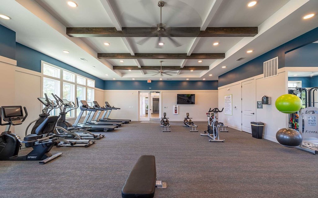 A gym with a variety of exercise equipment including treadmills, stationary bikes, and weights.