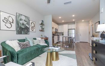 A living room with a green velvet couch, a glass coffee table, and a lamp.