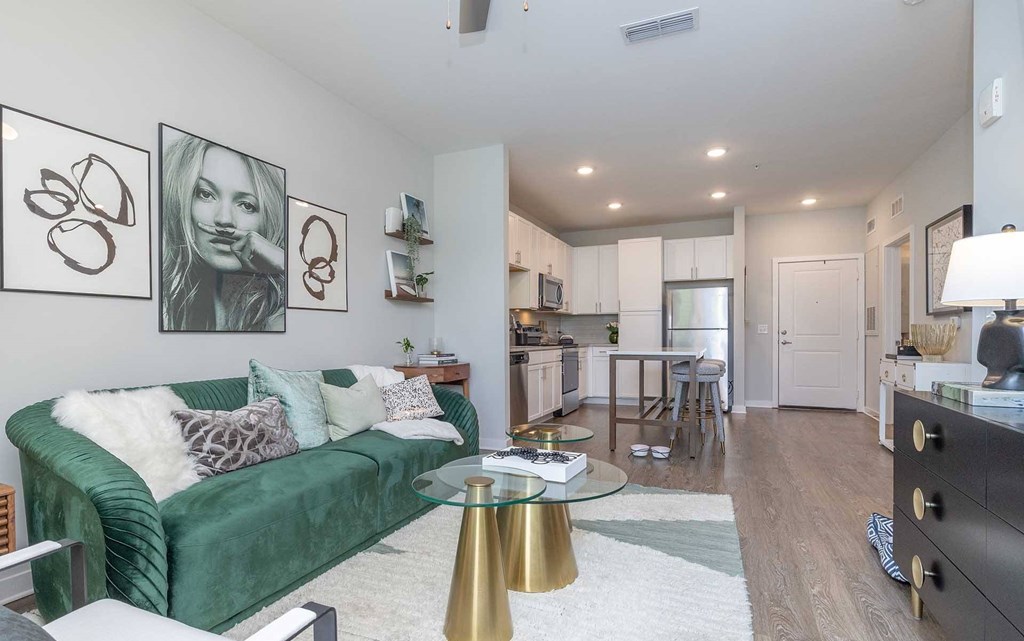 A living room with a green velvet couch, a glass coffee table, and a lamp.