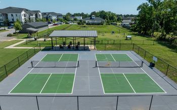 A tennis court with a green surface and a black fence surrounding it.