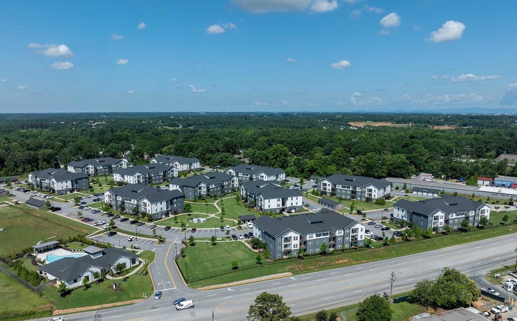 A large apartment complex is surrounded by trees and a highway.