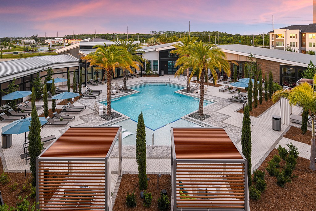 an aerial view of a resort style pool with palm trees and umbrellas