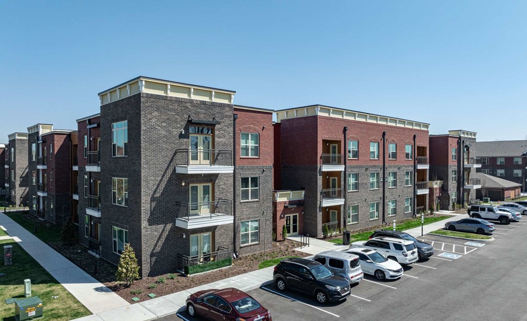 A row of apartment buildings with cars parked in front.