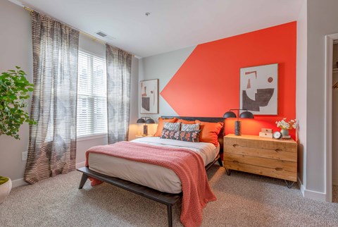 a bedroom with an orange accent wall and a bed with a wooden dresser and bedside
