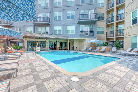a swimming pool with lounge chairs and umbrellas in front of an apartment building