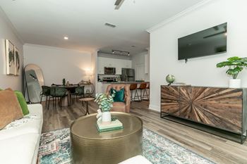 A modern living room with a white sofa, a wooden coffee table, and a flat-screen TV mounted on the wall.