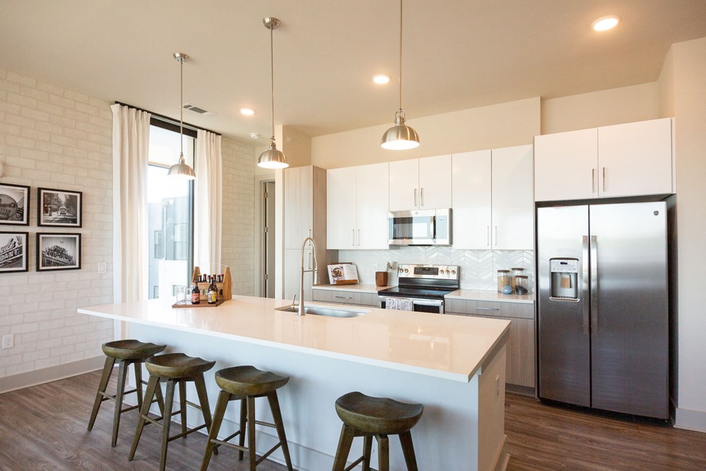 Luxury Apartments in Downtown Memphis TN - The Landing Residences - Spacious and Modern Kitchen with White Quartz Countertops, Stainless Steel Appliances, Geometric Tile Backsplash, Large Cooking Island with Seating and Hanging Overhead Lights, Hardwood Floor, and Light Cabinetry