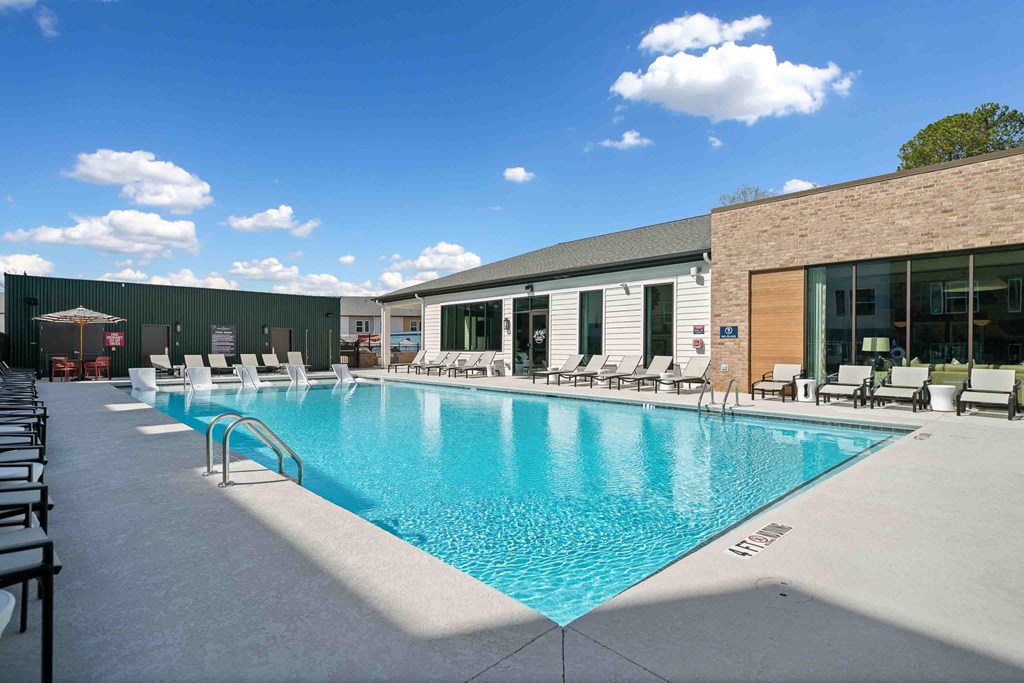 A large swimming pool with lounge chairs and a building in the background.