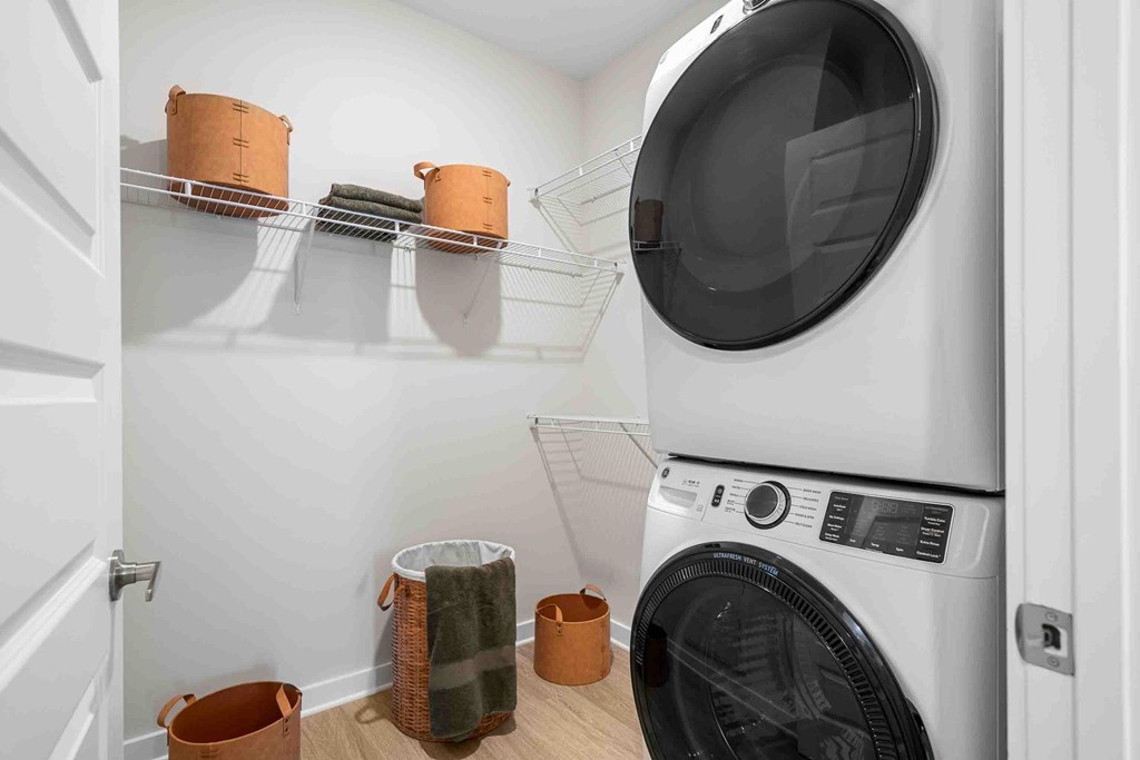 A washing machine is in a laundry room with a white door and a shelf with three baskets on it.