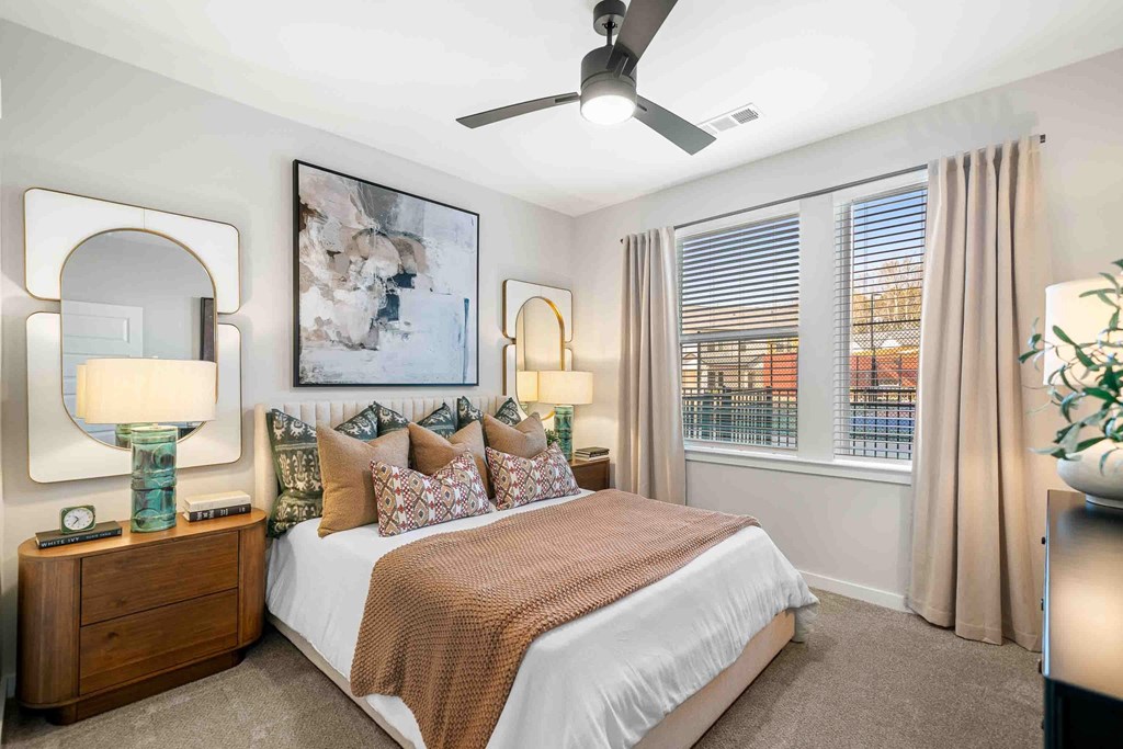 A bedroom with a large bed, a ceiling fan, and a painting on the wall.